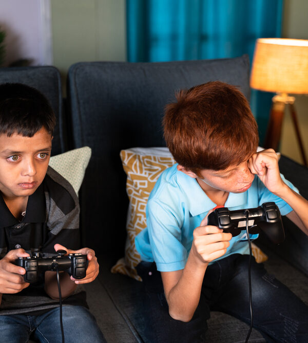 Parent Tips to Manage Eye Strain: concept of eye strain due to over night video game play - Two kids playing video game during late night at home and one kid rubbing his eyes due eye irritations.
